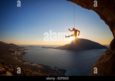 Kletterer hängen am Seil beim Vorstieg bei Sonnenuntergang mit Telendos Insel im Hintergrund Stockfoto