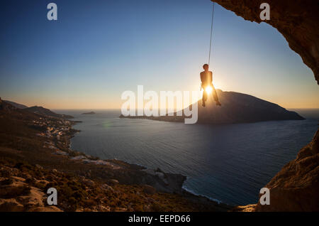 Kletterer hängen am Seil beim Vorstieg bei Sonnenuntergang mit Telendos Insel im Hintergrund Stockfoto