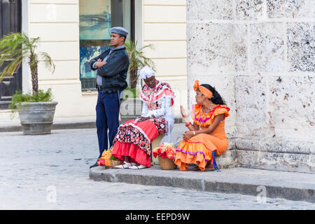 Einheimische Frauen in bunten traditionellen Kleidern für Tipps Verkauf von Blumen und ein Polizist auf dem Cathedral Square, Havanna, Kuba Stockfoto