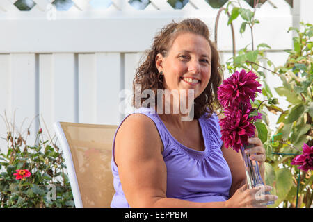 Frau mit Spina Bifida in Gartenterrasse entspannen und die Anpassung der Blumen Stockfoto