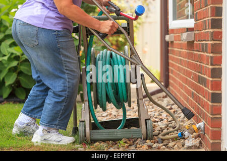 Frau mit Spina Bifida mit Krücken und ziehen Gartenschlauch Stockfoto