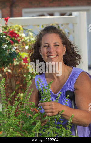 Frau mit Spina Bifida mit Krücken und schneiden Gartenblumen Stockfoto