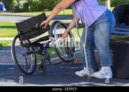 Frau mit Spina Bifida mit Krücken, um Rollstuhl auseinander zu nehmen, für die Reise im Auto Stockfoto