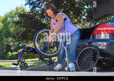 Frau mit Spina Bifida mit Krücken, um Rollstuhl auseinander zu nehmen, für die Reise im Auto Stockfoto