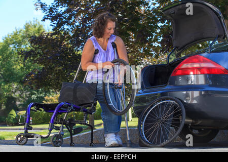 Frau mit Spina Bifida mit Krücken, um Rollstuhl auseinander zu nehmen, für die Reise im Auto Stockfoto