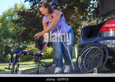 Frau mit Spina Bifida mit Krücken, um Rollstuhl auseinander zu nehmen, für die Reise im Auto Stockfoto