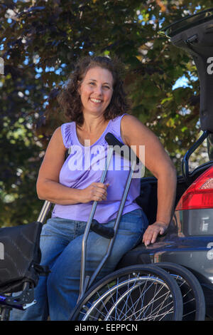 Frau mit Spina Bifida mit Krücken und relaxen am Auto Stockfoto