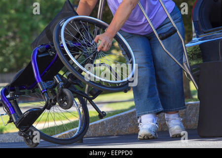 Frau mit Spina Bifida mit Krücken, um Rollstuhl auseinander zu nehmen, für die Reise im Auto Stockfoto