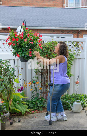 Frau mit Spina Bifida auf Krücken Befestigung Blumen im Sommer Stockfoto
