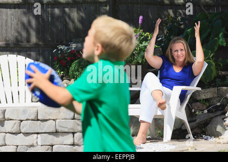 Mutter und Sohn mit Hörschädigungen Fußball spielen und Unterzeichnung in amerikanischer Gebärdensprache im Hinterhof Stockfoto