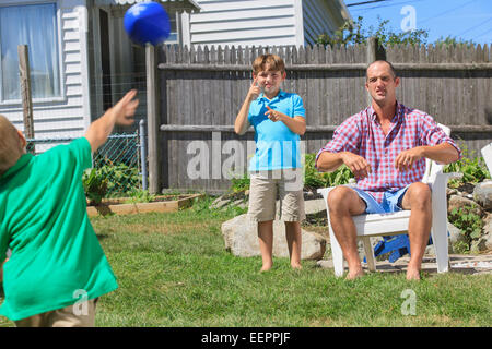 Vater und Söhne mit Hörschädigungen Fußball spielen und Unterzeichnung in amerikanischer Gebärdensprache im Hinterhof Stockfoto