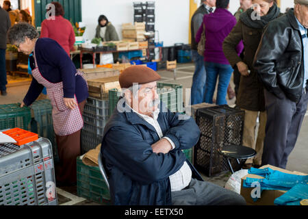 reifer Mann sitzt an seinem Stall verkaufen Obst & Gemüse auf einem Markt in Portugal Stockfoto