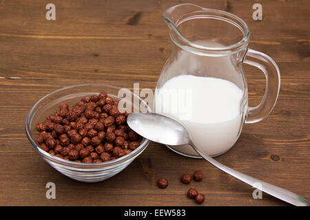 Schüssel mit Schokolade Getreide und Krug Milch auf Holztisch Stockfoto