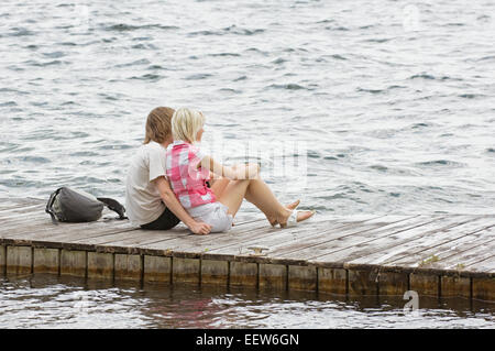 Ein paar sitzt auf einem Dock Blick auf Wasser Stockfoto