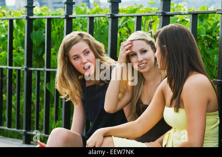 Drei Freundinnen mit Einkaufstüten sitzt auf einem Felsvorsprung und ein Gespräch Stockfoto