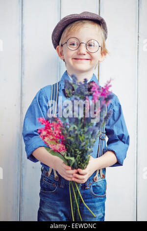 Niedliche kleine Junge in Freizeitkleidung und Brillen mit Wildblumen Stockfoto