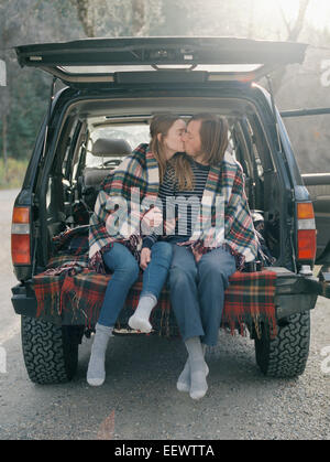 Junges Paar sitzt auf der Rückseite ihres Autos, küssen. Stockfoto