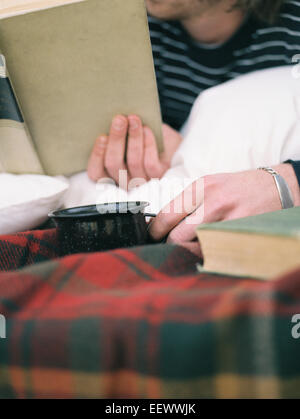 Der junge Mann ein Buch lesen, hält einen Becher hautnah. Stockfoto