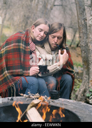 Junges Paar sitzt an einer Feuerstelle, in eine Decke gehüllt. Stockfoto