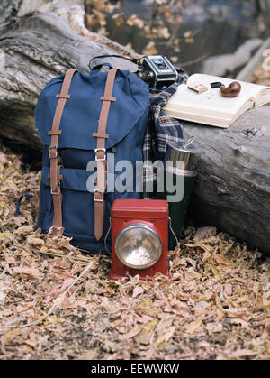 Wandern Ausrüstung, Rucksack, Taschenlampe, Kolben und Kamera durch einen Baumstamm. Ein Rohr auf ein offenes Buch liegen. Stockfoto