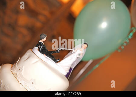 Braut und Bräutigam Figuren auf Hochzeitstorte mit grünen Ballon im Hintergrund Stockfoto