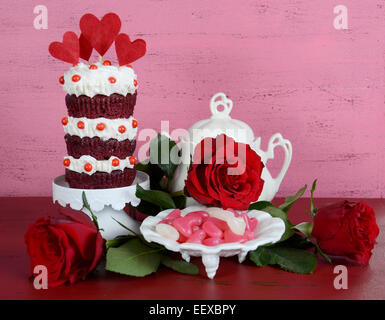 Vintage-Stil Dreischicht rote Velvet Cupcake auf weiße Kuchenplatte mit Rosen und Süßigkeiten im Hintergrund Vintage shabby chic, Stockfoto