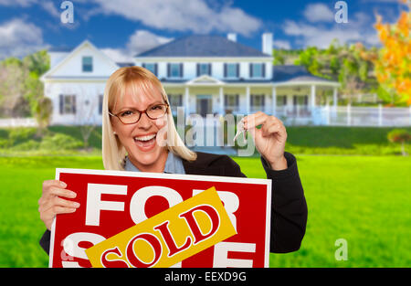 Erregte Frau hält Hausschlüssel und verkauft Immobilien Schild vor schönes neues zu Hause. Stockfoto