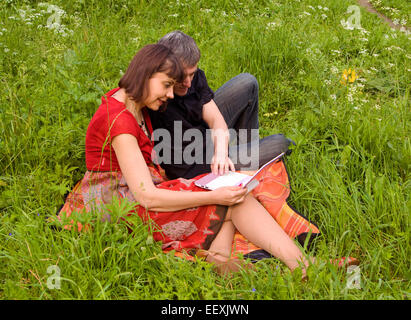 Junges Paar Mann und Frau mit Notebook (Laptop) auf grünen Rasen Wiese sitzen. Stockfoto