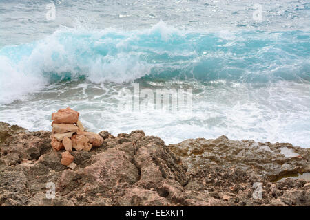 Klare, türkisfarbene Wellen plätschern auf wenig Steinturm und Ufer am Cap de Ses Salines, Mallorca Süd. Stockfoto