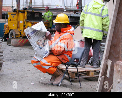 Bauarbeiter auf der Baustelle macht eine Pause. Builder liest täglich Telegraph während der Mittagspause in Hardhut mit Ohrenschützern Stockfoto