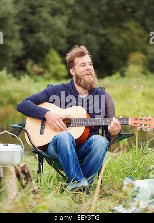 lächelnder Mann mit Gitarre und Dixie im camping Stockfoto