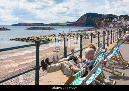 Sidmouth, Devon, UK - Leute sitzen in Liegestühlen am Meer im Sommer Stockfoto