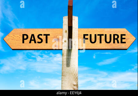 Wegweiser aus Holz mit zwei entgegengesetzte Pfeile über klaren, blauen Himmel, Vergangenheit versus Zukunft Nachrichten, Mentalität Konzeptbild Stockfoto