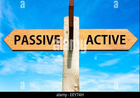 Wegweiser aus Holz mit zwei entgegengesetzte Pfeile über klaren, blauen Himmel, passiv im Vergleich zu aktiven Nachrichten, Lebensstil zu ändern, Konzeptbild Stockfoto