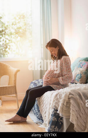 Schwangere Frau auf dem Bett sitzend Stockfoto