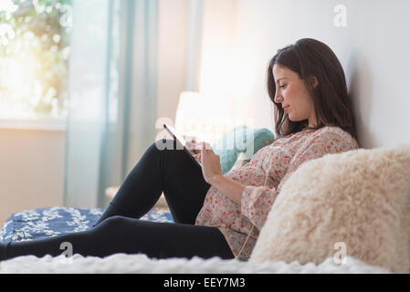 Schwangere Frau sitzen auf Bett mit tablet Stockfoto