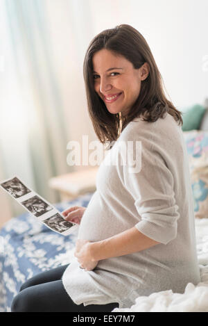 Schwangere Frau mit Ultraschall, sitzt auf dem Bett lächelnd Stockfoto