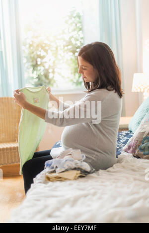 Schwangere Frau sitzen auf Bett beobachten Baby Kleidung Stockfoto