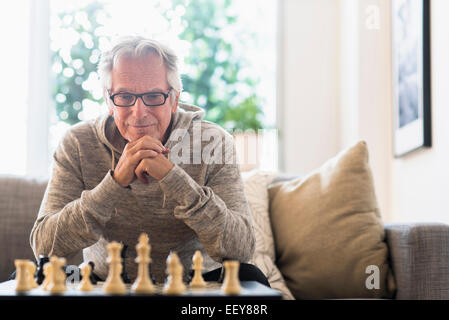 Ältere Mann sitzt im Wohnzimmer und spielt Schach Stockfoto