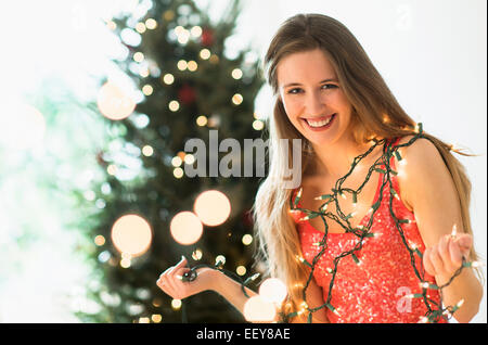 Porträt der jungen Frau schmücken Weihnachtsbaum mit Weihnachtsbeleuchtung Stockfoto