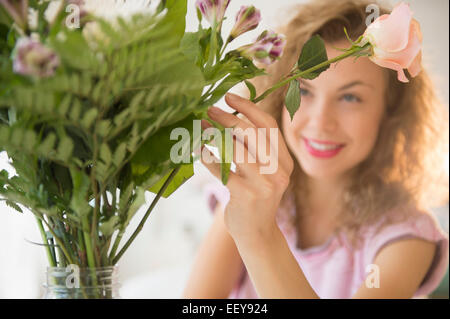 Lächelnde junge Frau setzen Blumen in vase Stockfoto