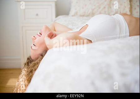 Junge Frau auf dem Bett liegend und lachen Stockfoto