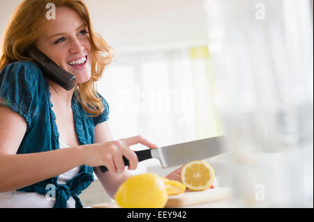 Junge Frau Zitrone schneiden und am Telefon Stockfoto