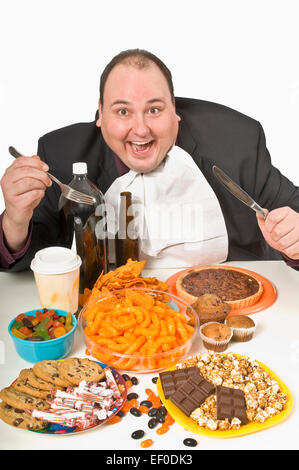 Übergewichtiger Mann sitzt an einem Tisch voller Junk-food Stockfoto