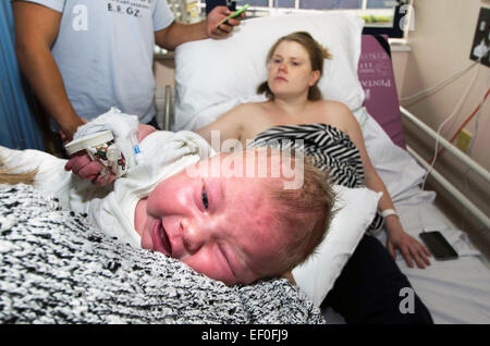 Ein neugeborenes Baby durch eine Krankenschwester mit ihrer Mutter in einem Krankenhausbett direkt hinter ihr sitzt statt. Stockfoto