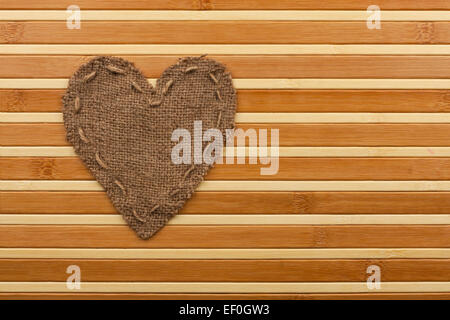 Das symbolische Herz der Sackleinen liegt auf einer Bambusmatte als Hintergrund Stockfoto