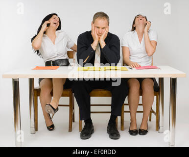 Frustriert Mann sitzt am Schreibtisch mit Frauen am Telefon Stockfoto