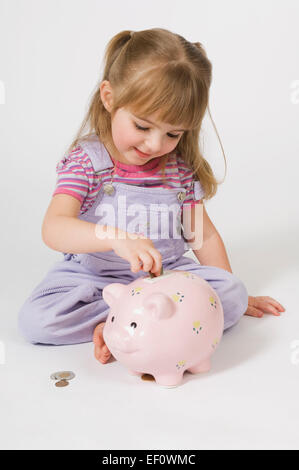 Junges Mädchen setzen Münzen in ein Sparschwein Stockfoto