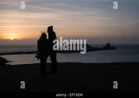 Wanderer-Silhouette bei Sonnenuntergang an einem bitter kalten, sonnigen und windigen Tag in Wurm Kopf, Rhossili Strand Bucht, Halbinsel Gower, Wales, UK, Stockfoto