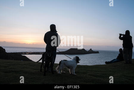 Dog Walker Silhouette mit zwei Hunden bei Sonnenuntergang an einem bitter kalten, sonnigen und windigen Tag des Wurms Kopf, Gower Halbinsel, Wales, UK. Stockfoto